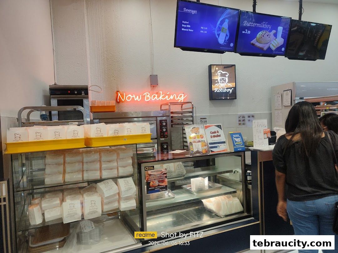 Interior view of a RotiBoy bakery with baked goods displayed and digital menus overhead.