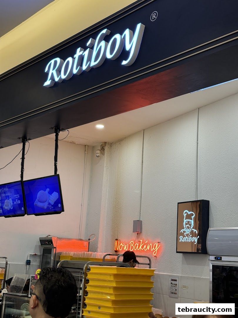 The Rotiboy shop front with illuminated signage and a 'Now Baking' neon sign.