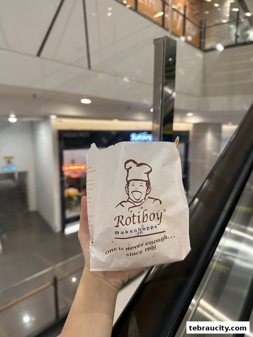 A hand holds a Rotiboy paper bag with the brand logo and slogan.