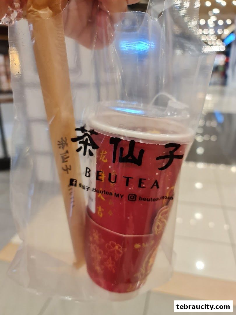 A person holds a plastic bag containing a red cup with a drink and a straw.