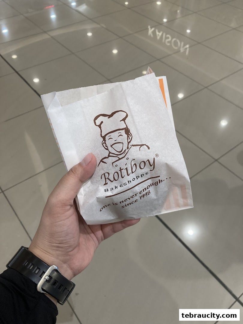 A hand holds a Rotiboy paper bag with the brand logo and slogan.