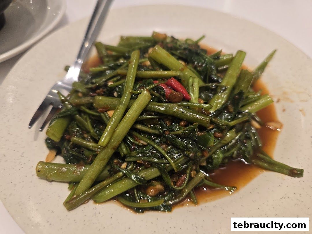 A plate of stir-fried water spinach with chili and garlic, served with a fork.