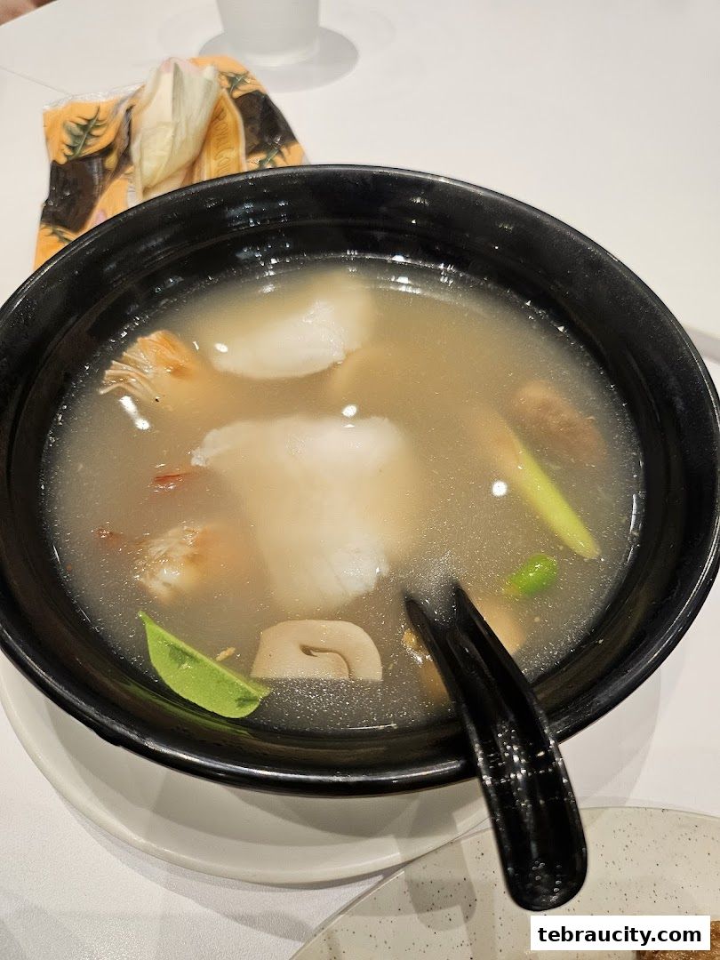 A close-up of a steaming bowl of soup with seafood and vegetables, served with a black spoon.