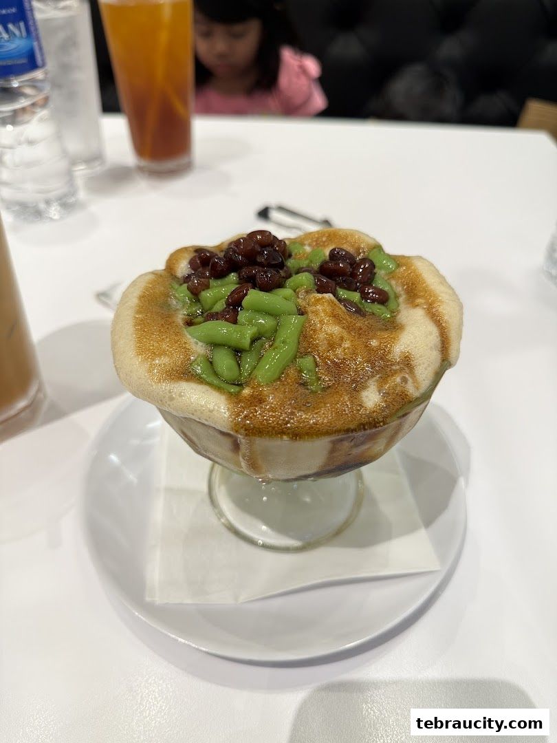 A close-up of a dessert with green jelly, red beans, and a creamy topping.
