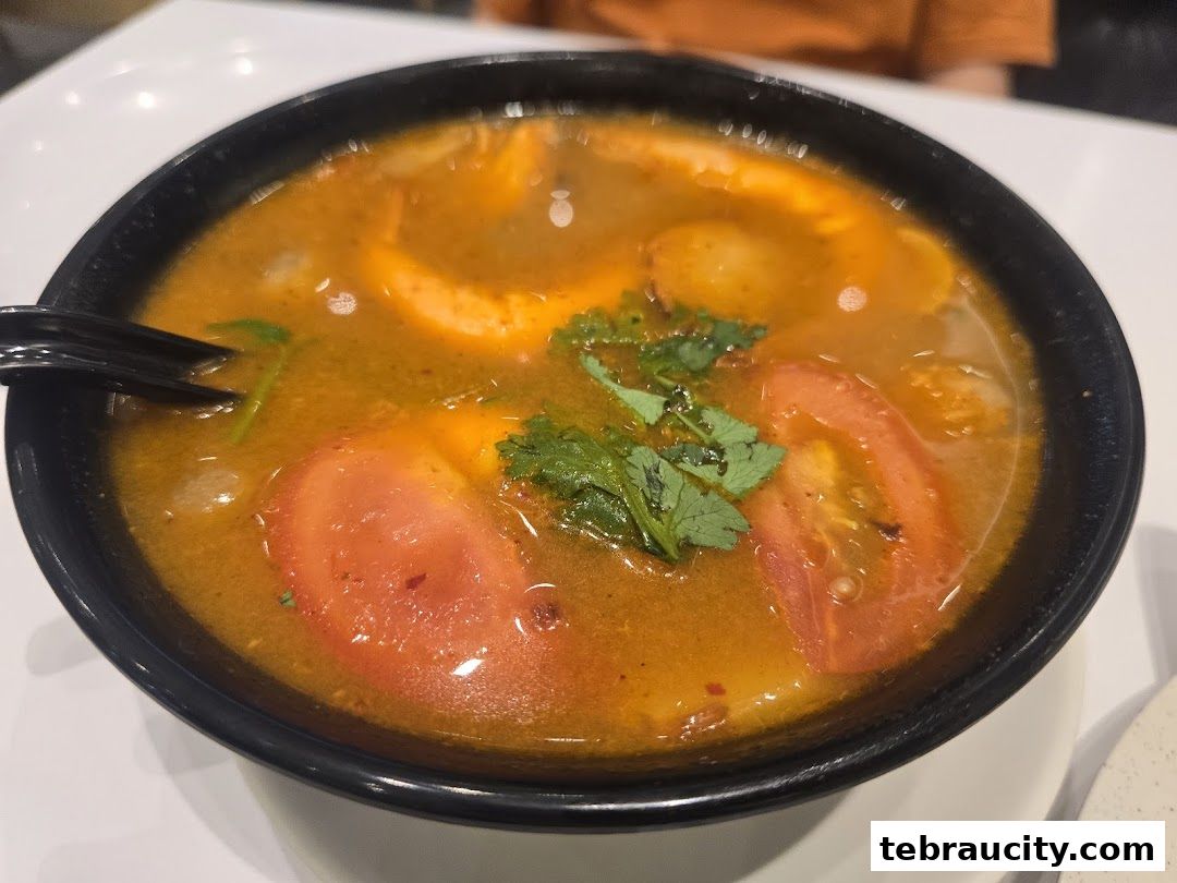 A close-up shot of a steaming bowl of Tom Yum soup with prawns and tomatoes.