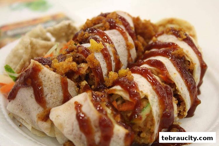 A close-up shot of delicious spring rolls drizzled with sauce and topped with crispy bits.