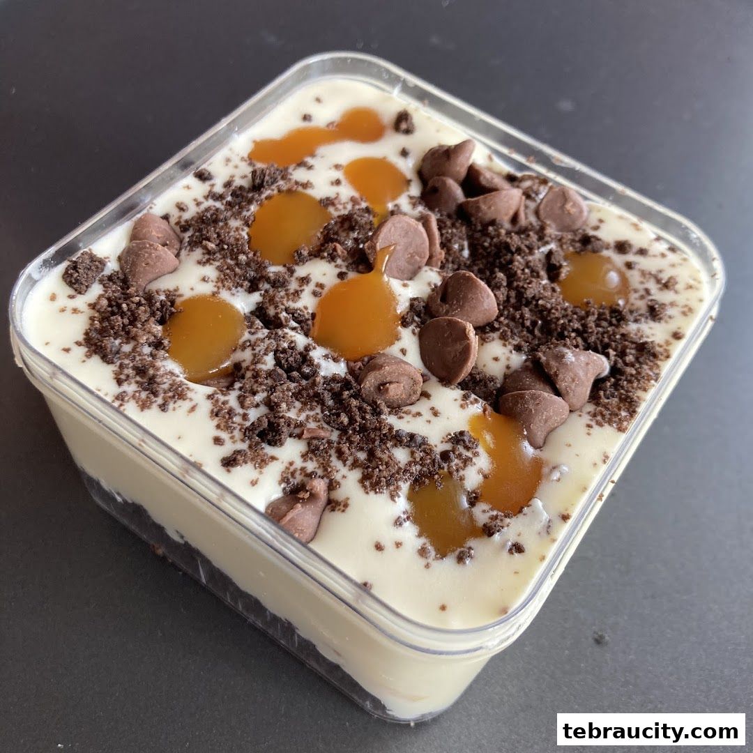 A delicious dessert in a clear container, topped with chocolate chips, cookie crumbs, and caramel.