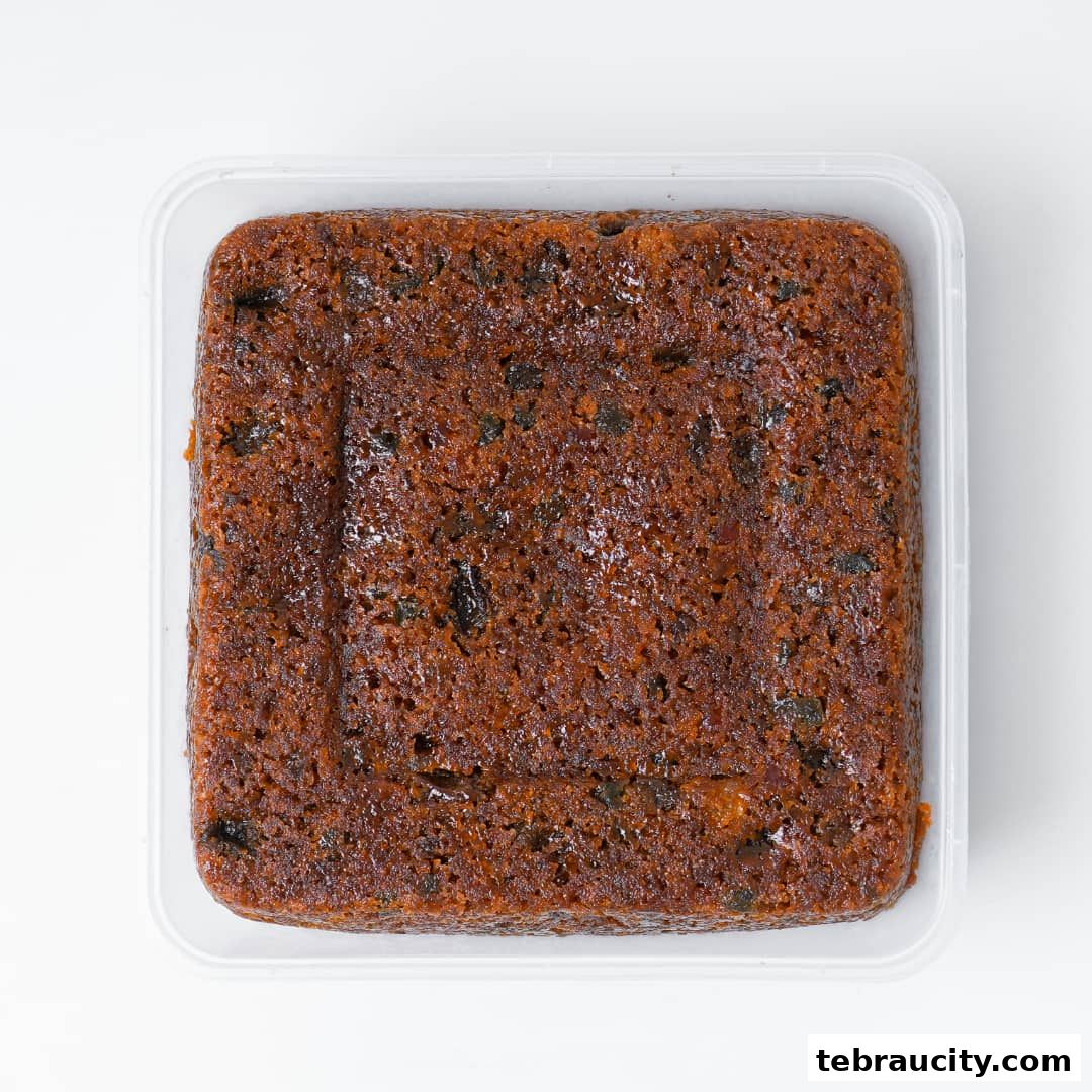 A square fruitcake with visible dried fruits in a clear plastic container.