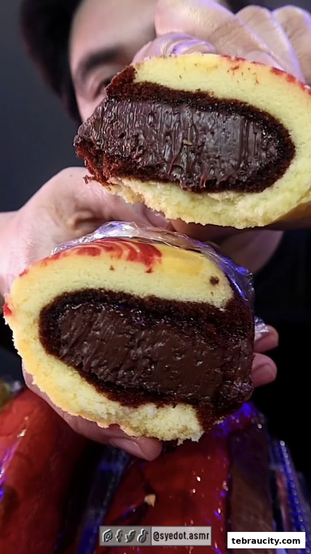A person holds a sliced dessert with rich chocolate filling and a light sponge cake.