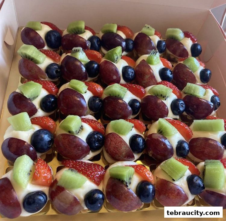 A box filled with mini fruit tarts topped with cream, strawberries, blueberries, grapes, and kiwi.