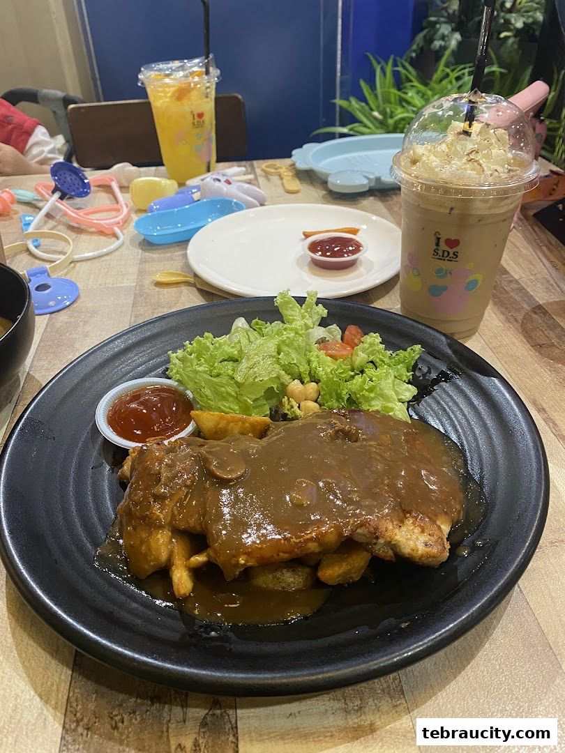 A plate of chicken steak with fries and salad, accompanied by drinks and toys on a table.