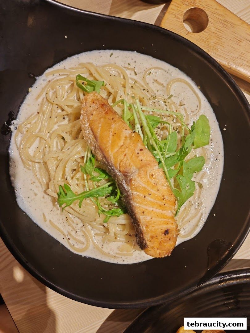 A close-up shot of creamy pasta topped with a piece of pan-seared salmon and greens.