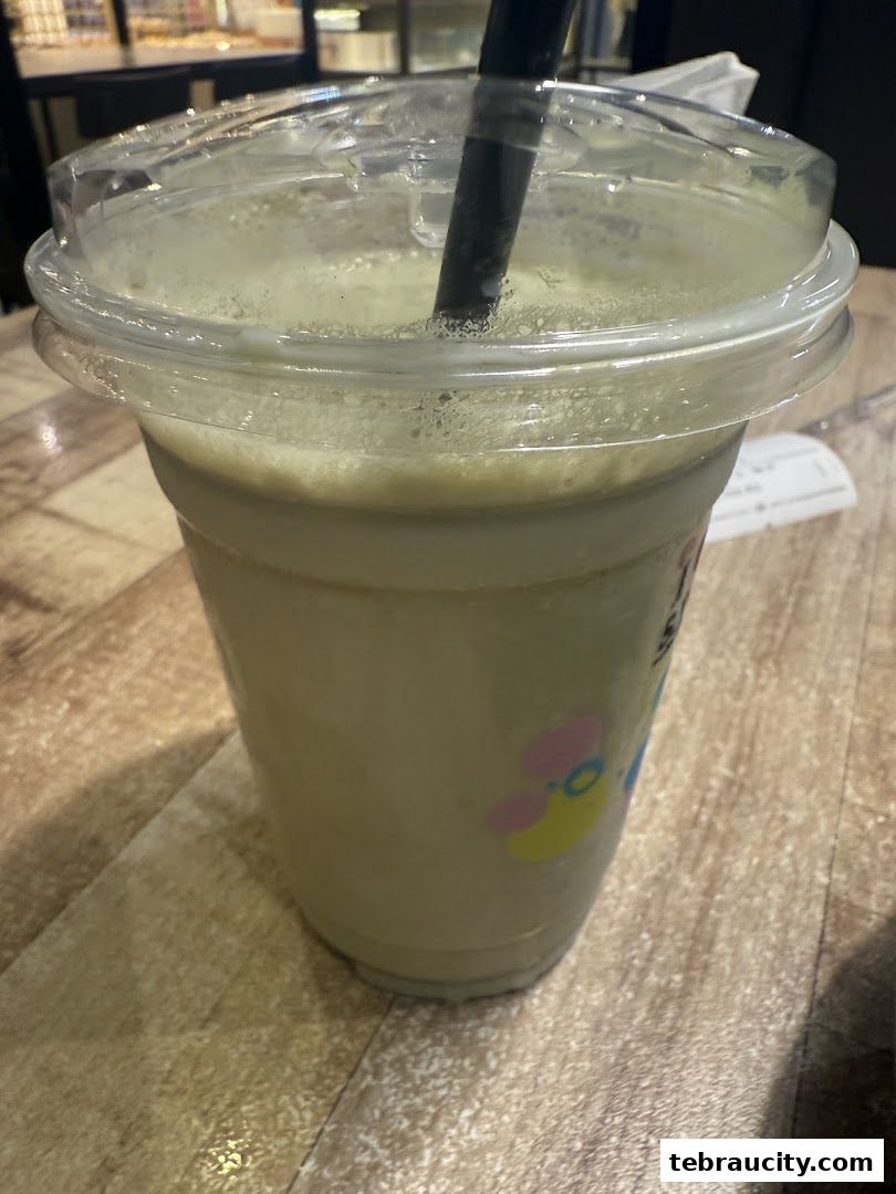 A close-up of a green beverage in a clear plastic cup with a straw.
