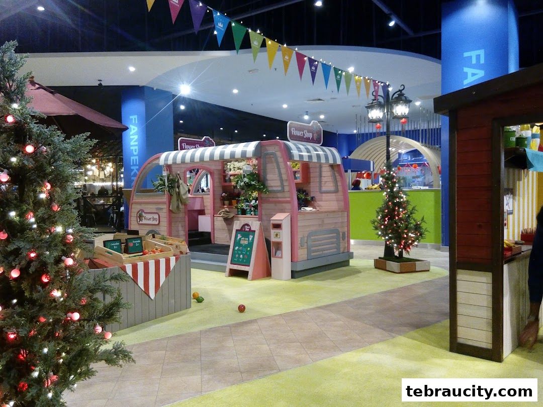 A festive display featuring a pink flower shop stall, Christmas trees, and market stalls in a mall.