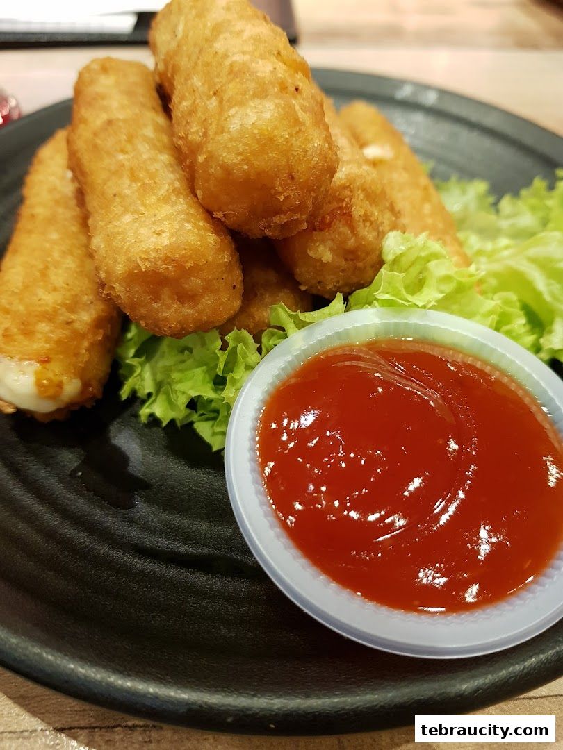 Golden fried mozzarella sticks served with ketchup and lettuce on a black plate.