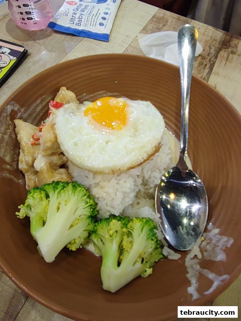 A close-up of a rice dish with a fried egg, chicken, and broccoli, served with a spoon.