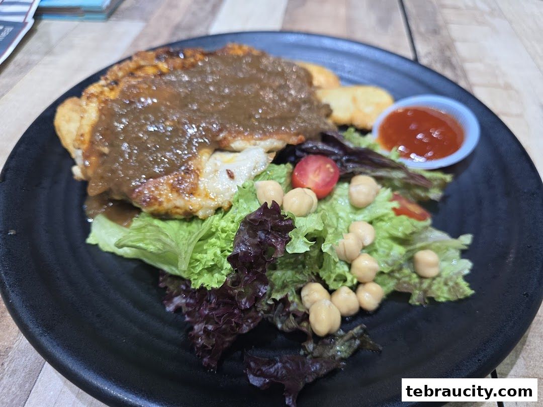 A close-up of a delicious chicken chop with salad, chickpeas, and sauce on a black plate.