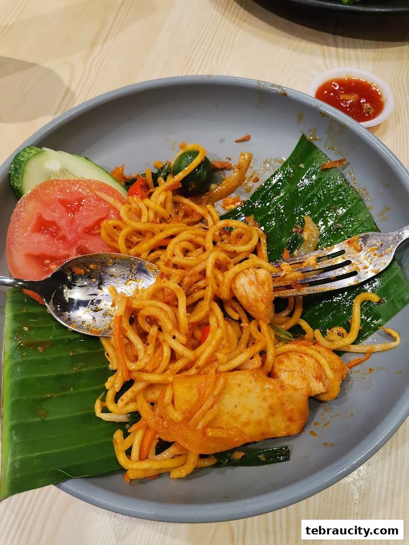 A plate of noodles with chicken, vegetables, and a side of chili sauce.