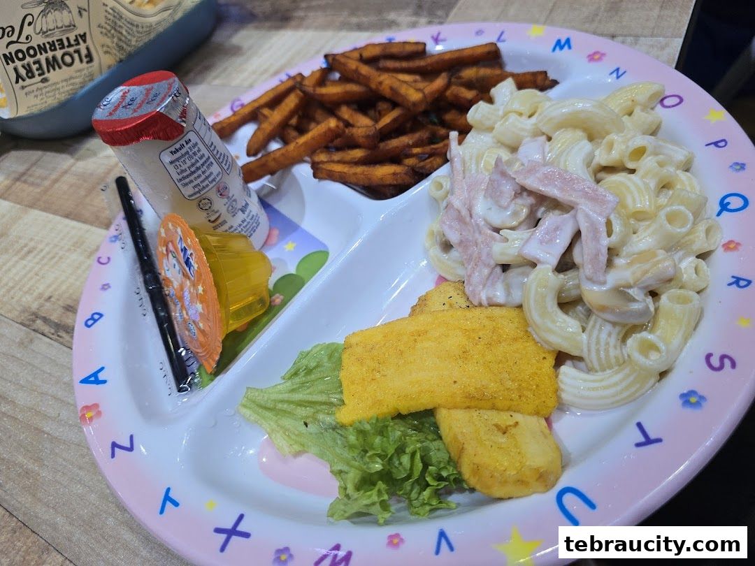 A child's meal with macaroni, fries, fish fingers, yogurt, and jelly.