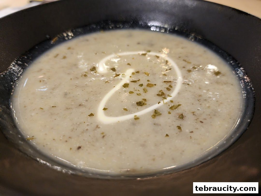 A close-up shot of a creamy mushroom soup with a swirl of cream and herbs.