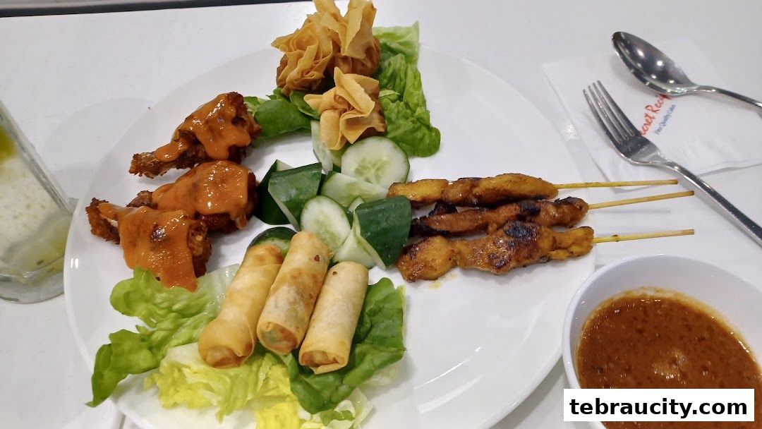 A plate of assorted appetizers including chicken wings, spring rolls, satay, and wontons with dipping sauce.