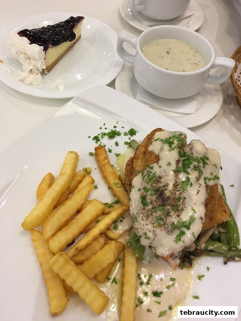 A delicious meal featuring fried fish, fries, soup, and a slice of blueberry cheesecake.