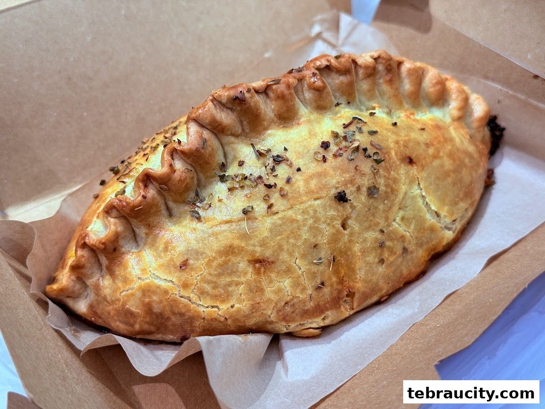 A golden-brown pastry with herbs, served in a brown paper box.