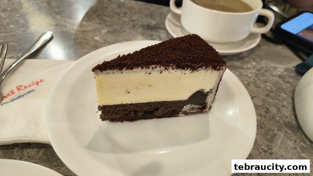 A slice of layered chocolate and cream cake with a coffee cup and napkin.