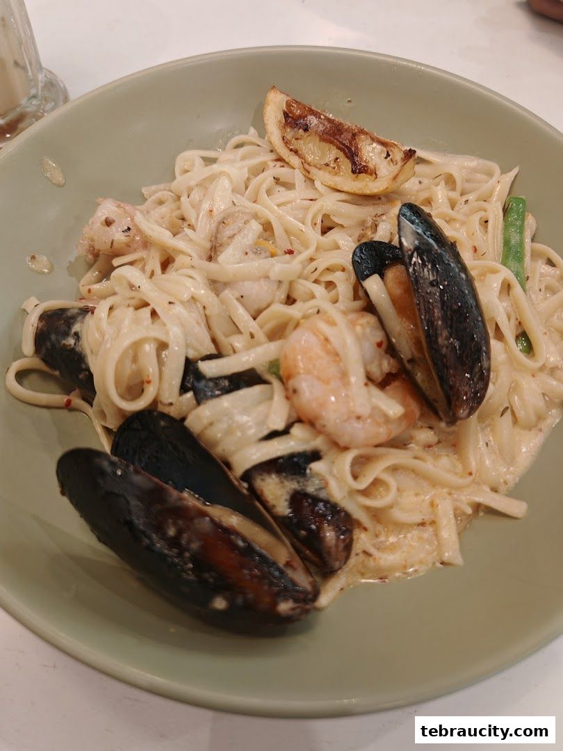 A close-up of a creamy seafood pasta dish with mussels, shrimp, and a lemon slice.
