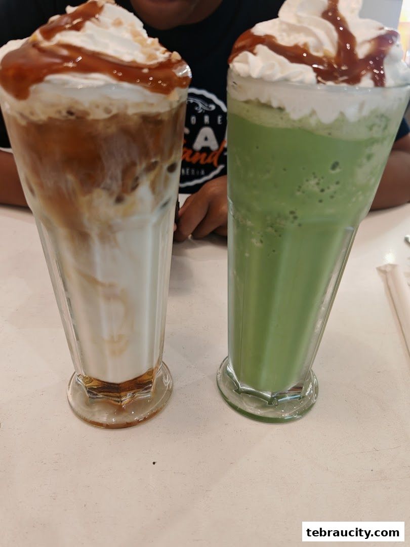 Two tall glasses of iced drinks, one caramel coffee and one green matcha, topped with whipped cream and caramel drizzle.
