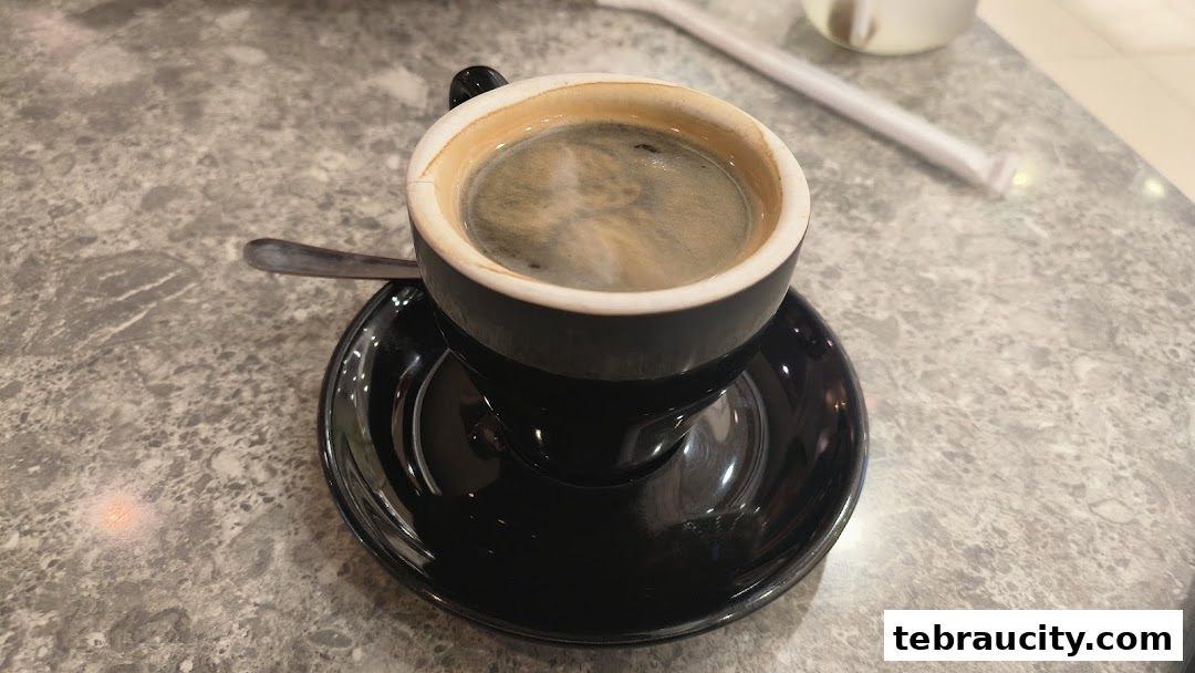 A close-up shot of a steaming cup of black coffee on a saucer with a spoon.