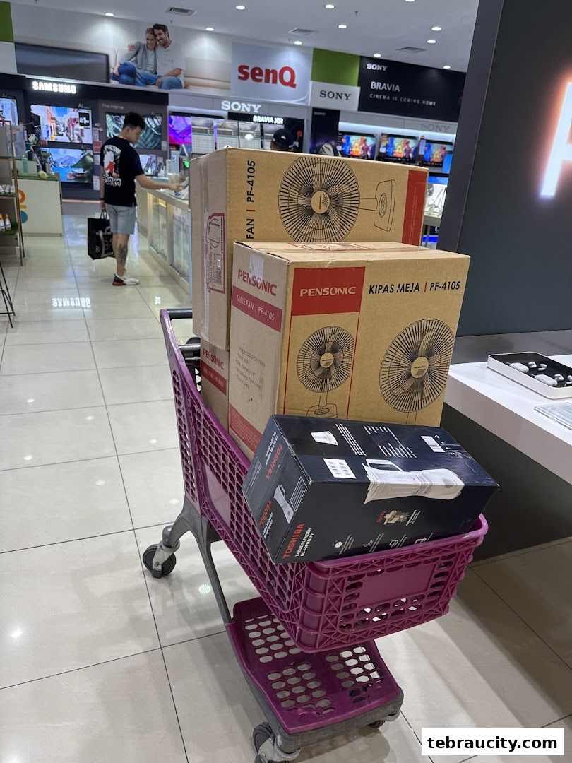 A shopping cart filled with boxes of fans and a blender in an electronics store.