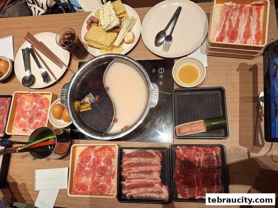 A table set for a hot pot meal with various meats, vegetables, and a yin-yang broth.