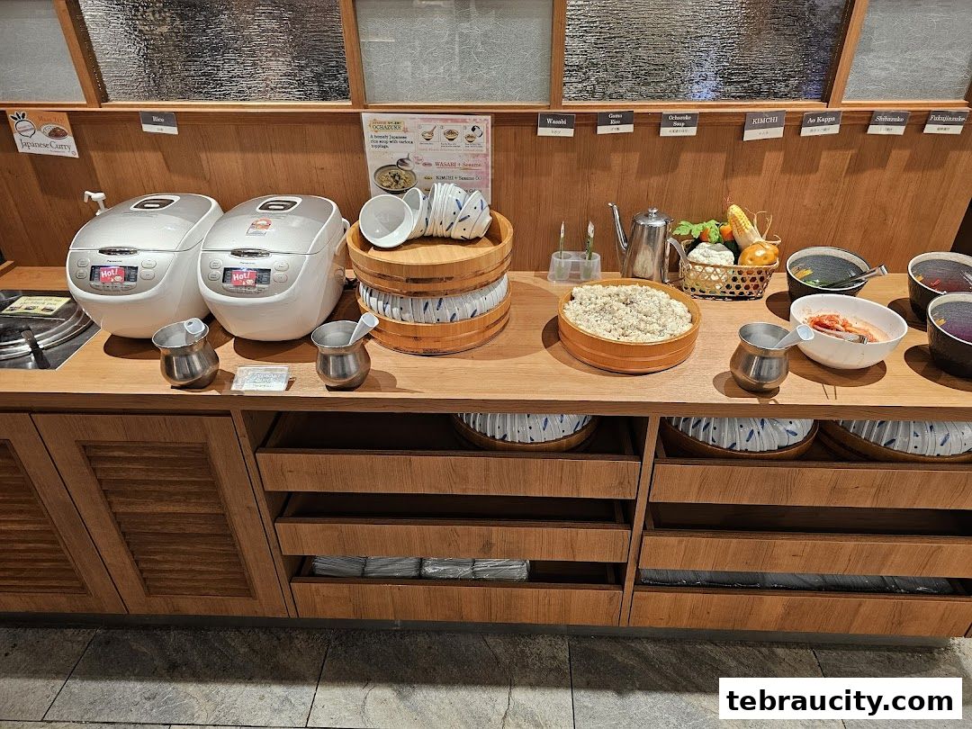 A buffet counter with rice cookers, bowls, and various Japanese dishes.