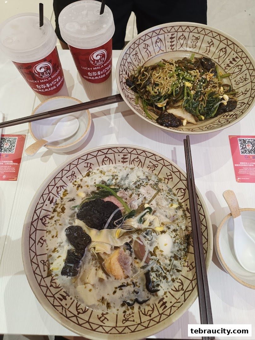Two bowls of mala noodles and drinks are served at a table.