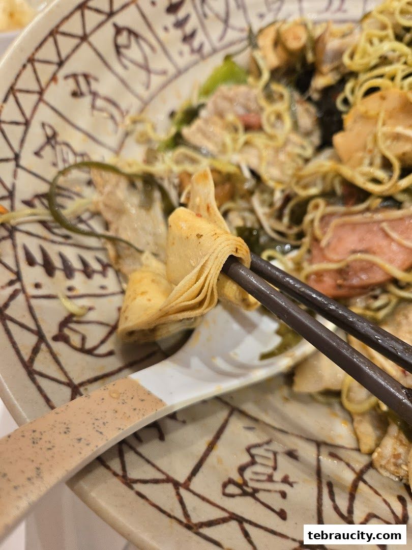 A close-up shot of a bowl of mala noodles being eaten with chopsticks and a spoon.