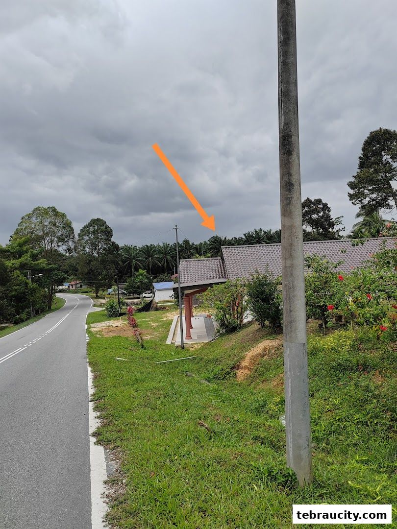 A road curves past a grassy slope towards a building with a covered entrance.
