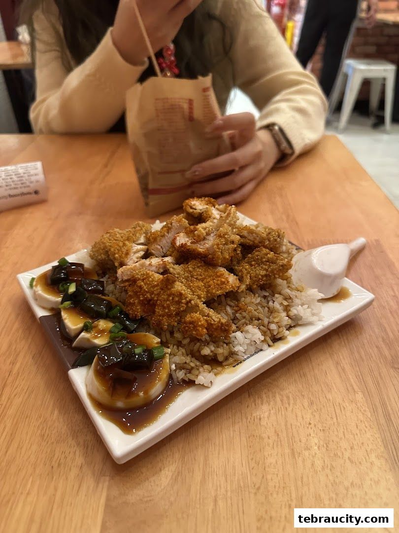 A plate of Taiwanese fried chicken with rice and preserved egg tofu is served on a wooden table.