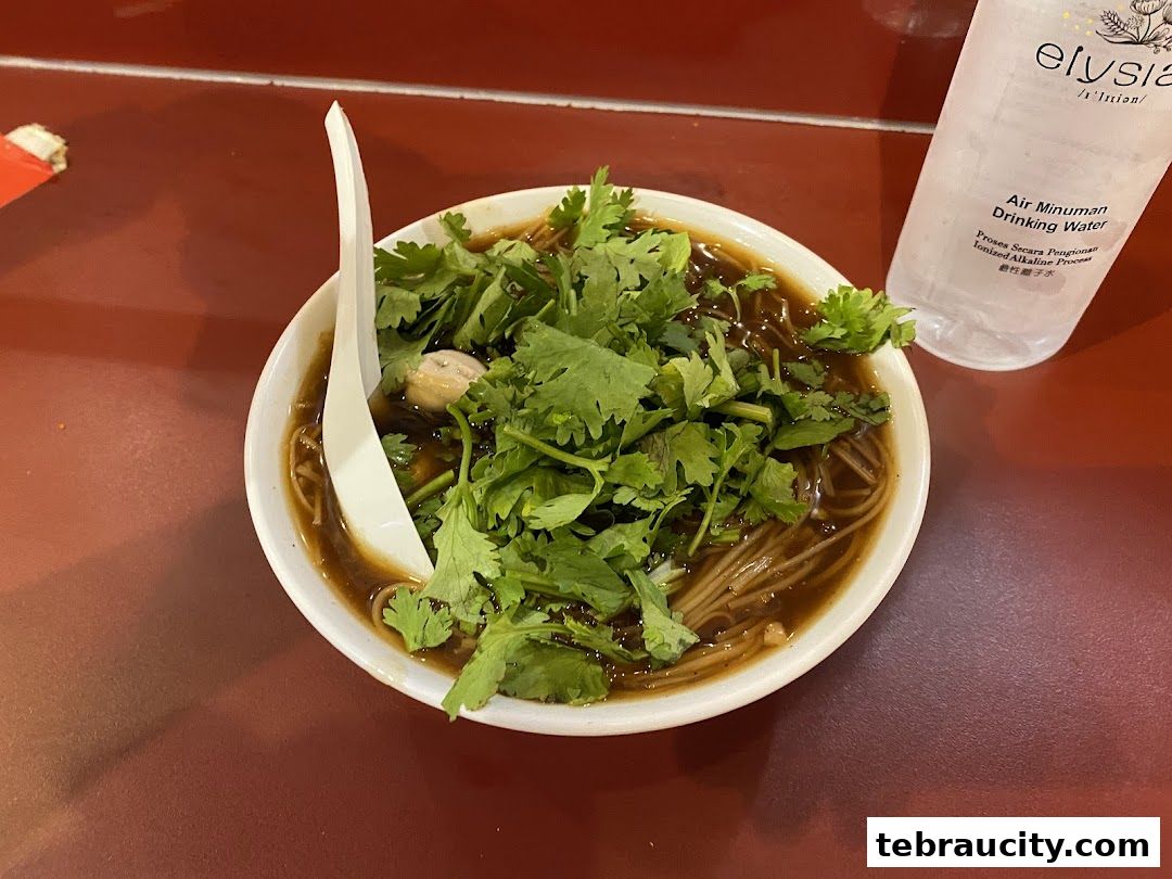 A bowl of Taiwanese oyster vermicelli topped with fresh cilantro and a spoon, next to a bottle of water.