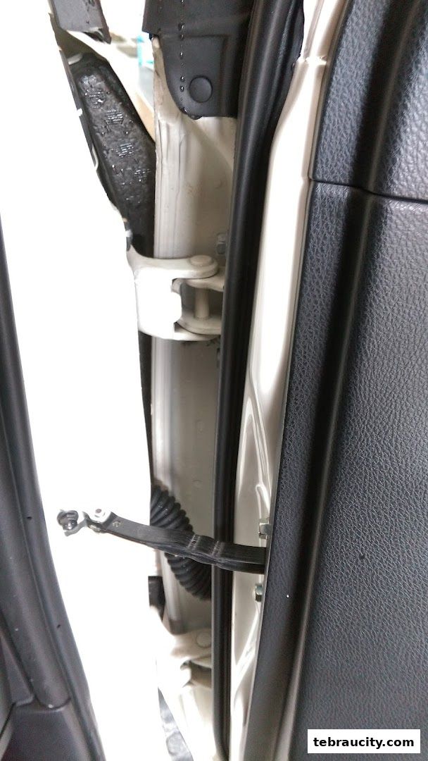 Close-up view of a car door hinge and interior paneling.