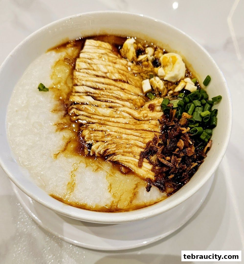 A bowl of Hainanese chicken congee topped with shredded chicken, egg, and scallions.