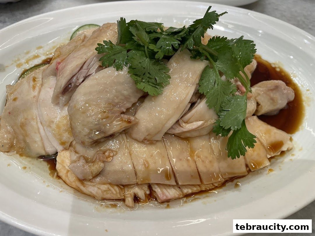 A plate of succulent Hainanese chicken rice, garnished with fresh cilantro and cucumber slices.