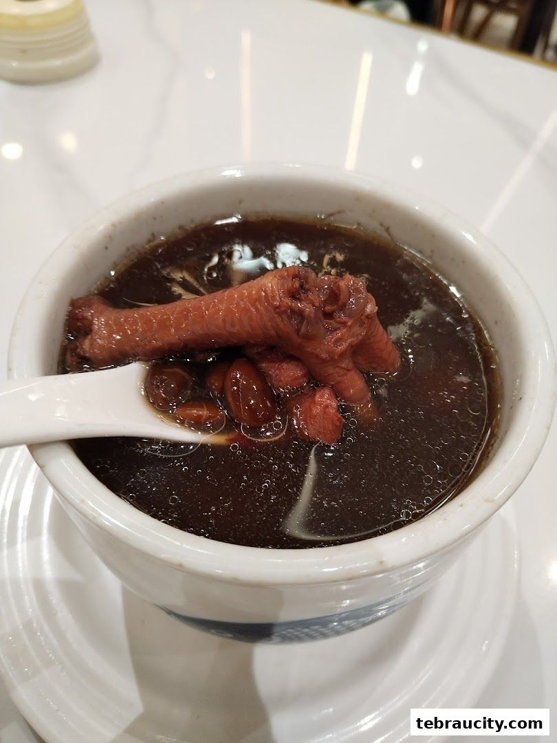 A close-up shot of a bowl of dark herbal soup with chicken feet and goji berries.