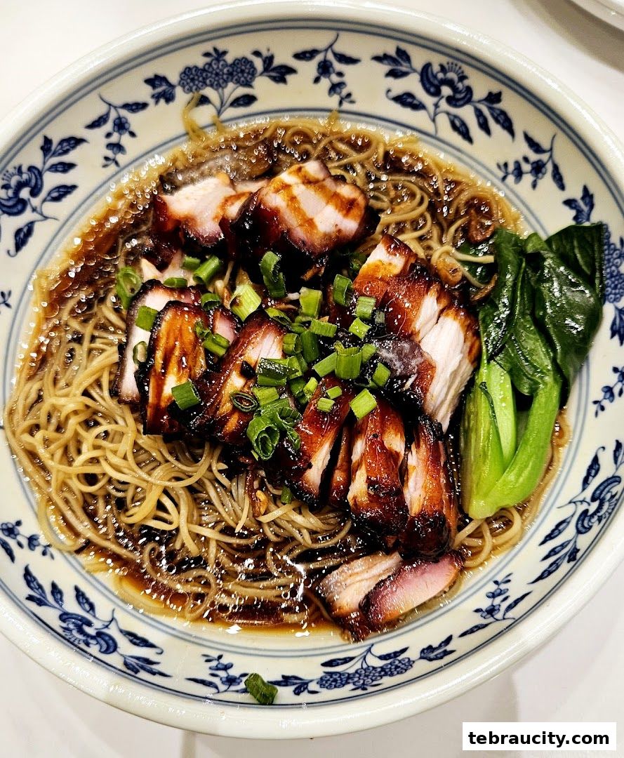 A close-up shot of a bowl of delicious char siu noodles with greens.