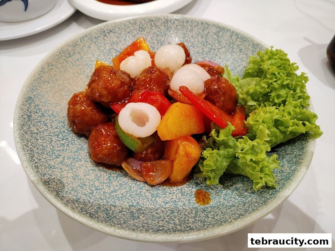 A close-up of a delicious dish with meatballs, lychees, and vegetables on a patterned plate.
