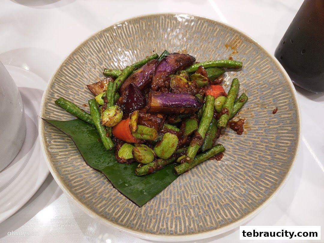 A plate of stir-fried vegetables including eggplant, long beans, and petai with a savory sauce.