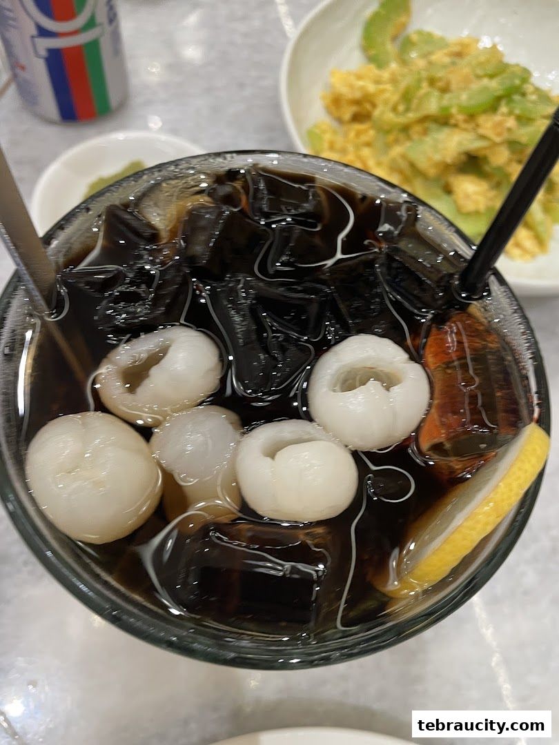 A refreshing drink with lychees, grass jelly, ice, and a lemon slice.