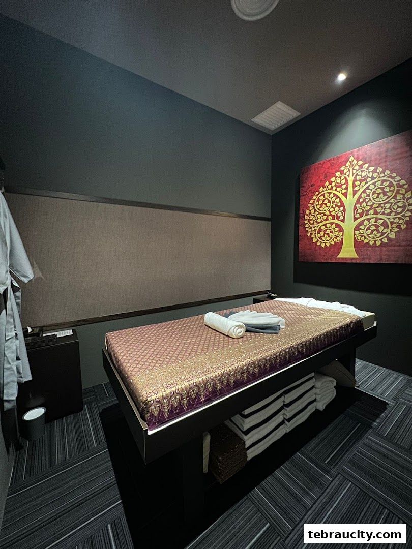 A massage room with a bed, towels, and a decorative tree painting on the wall.