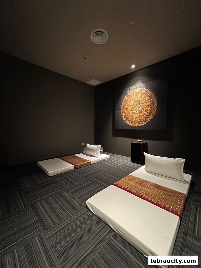 Two massage beds with pillows and decorative throws in a dimly lit room with a mandala artwork.