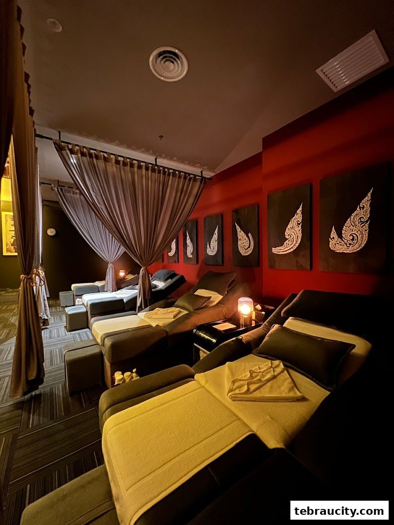 Comfortable reclining chairs with soft lighting and decorative Thai art on a red wall.